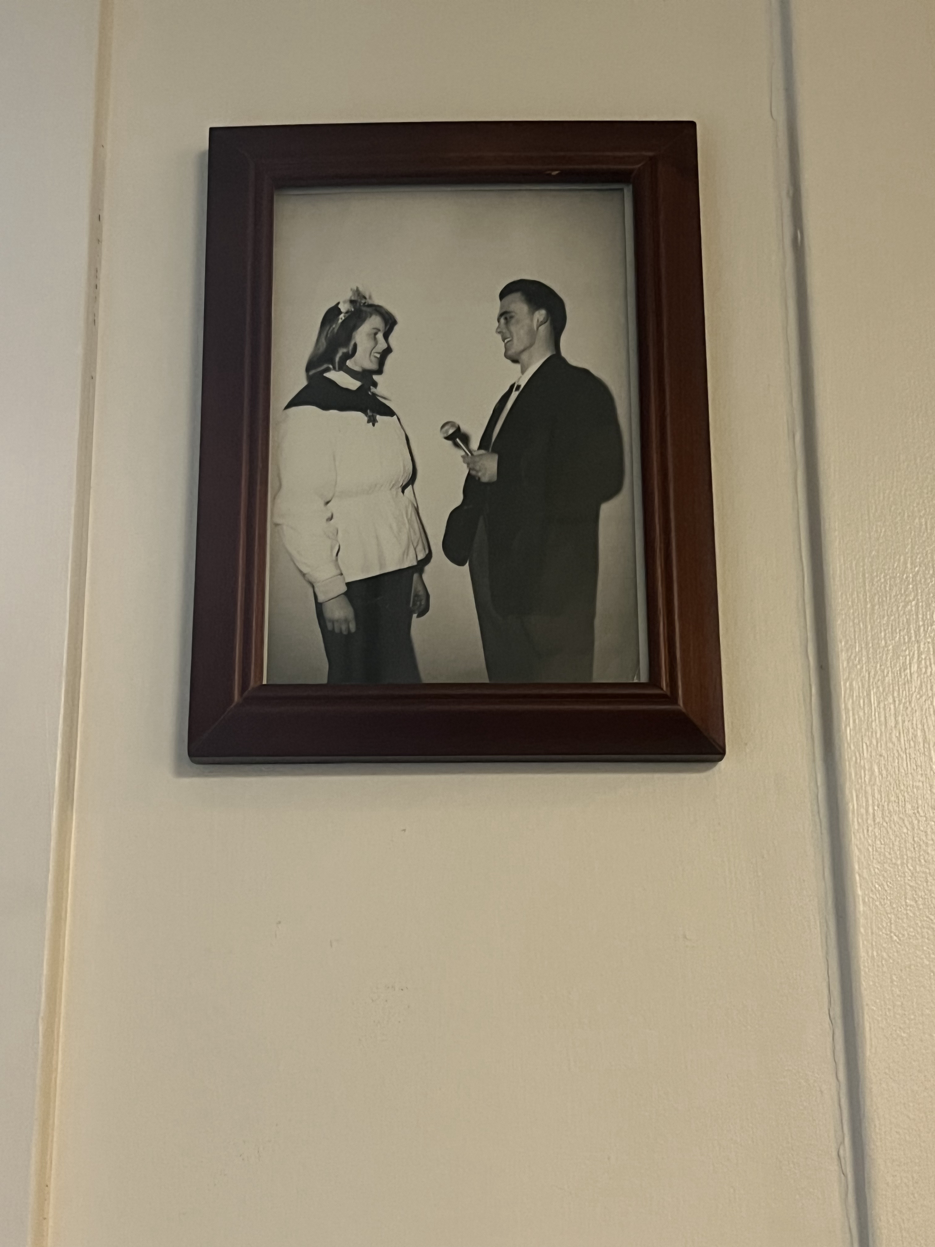 a feminine student in a cape and crown 
                and masculine student in a suit engage in conversation. 
                Their style seems to be from the 1950s, 
                and the photo is in black and white